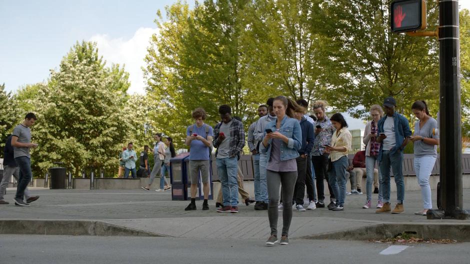 A woman crosses the street without looking up from her phone.