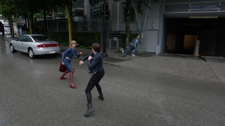 Kara and Malefic in the form of Alex fight on the street while a bystander runs for cover.