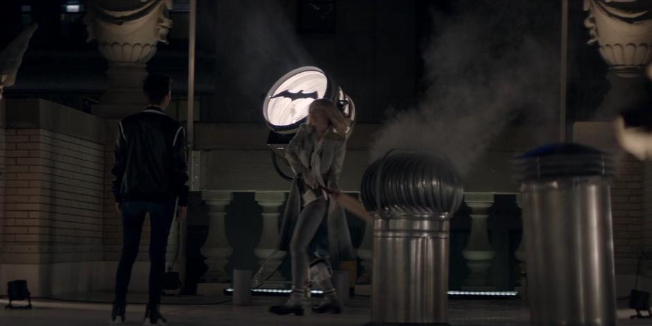 Kate watches as Alice swings her cricket bat at the Bat-Signal.