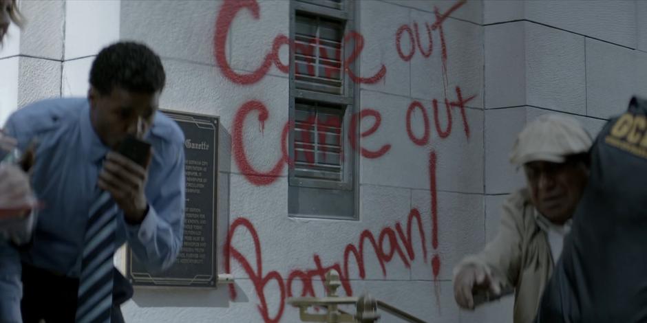 Graffiti on the wall of the building over the effigy calls out Batman.