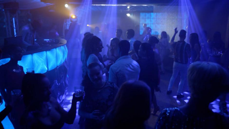 People dance and mingle in the blue light of the nightclub.
