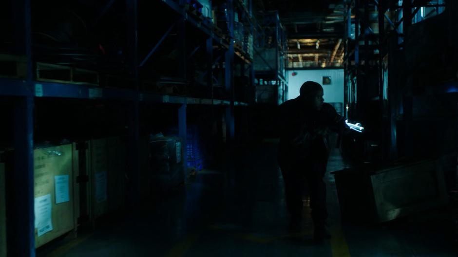 One of the gun smugglers searches the dark warehouse for the attacker.
