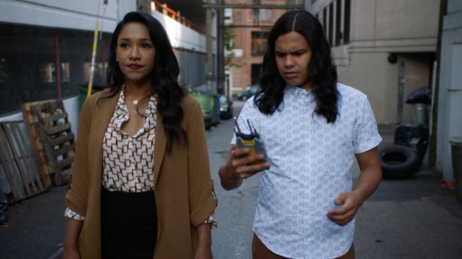 Cisco looks down at his tracker while walking through the alley with Iris.