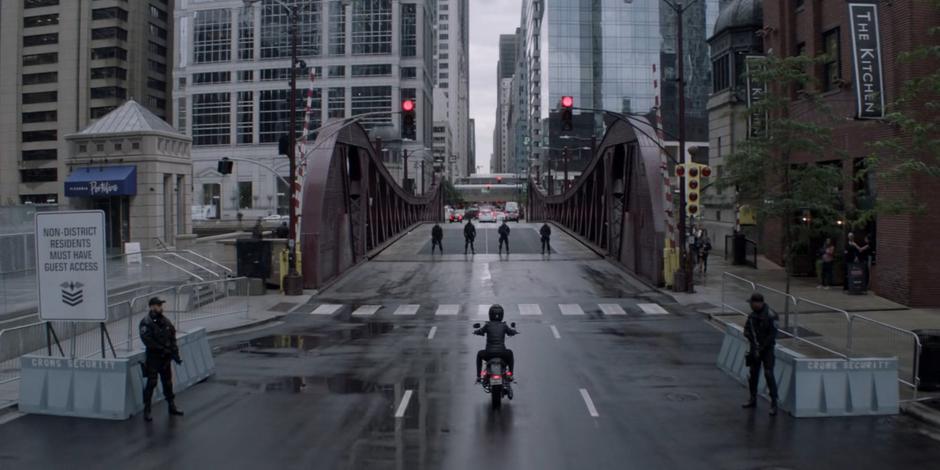 Kate rides her motorcycle towards the checkpoint into the Crows-controlled district.