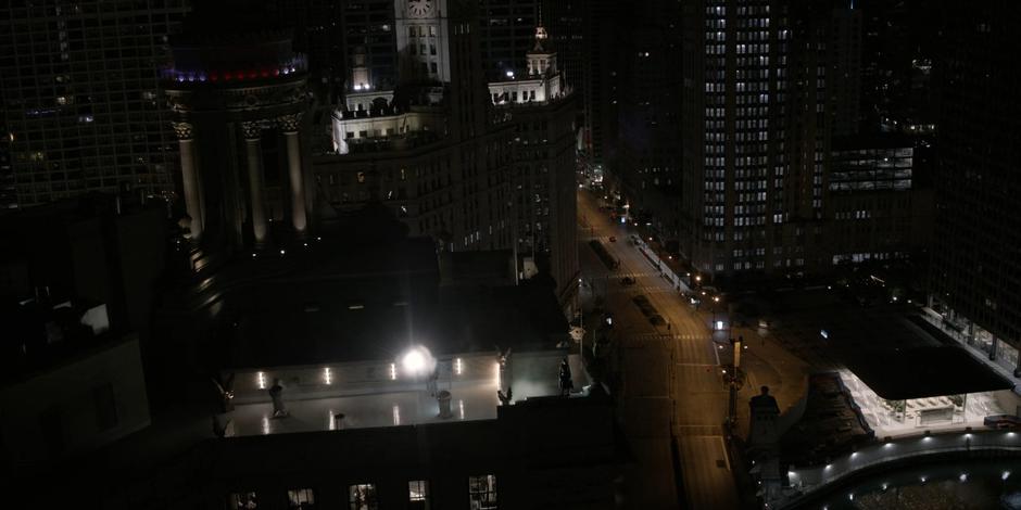 Kate stands on the edge of the rooftop as the new Bat-Signal shines into the sky past her.