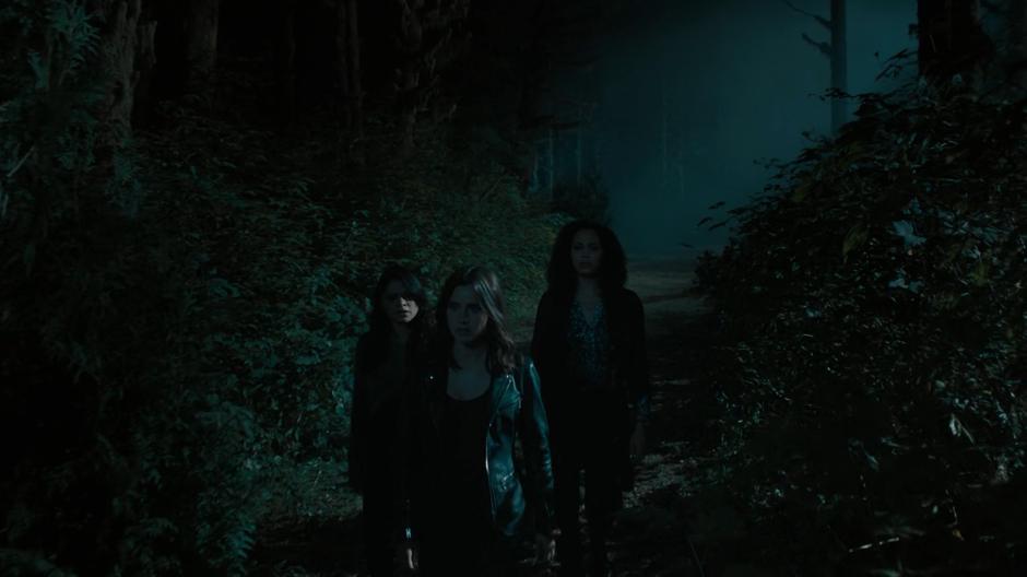 Mel, Abigael, and Macy walk down a path at night and see a light in the distance.