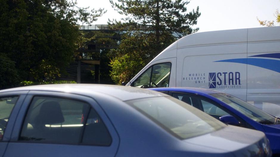 The S.T.A.R. Labs van sits in the parking lot outside the building.