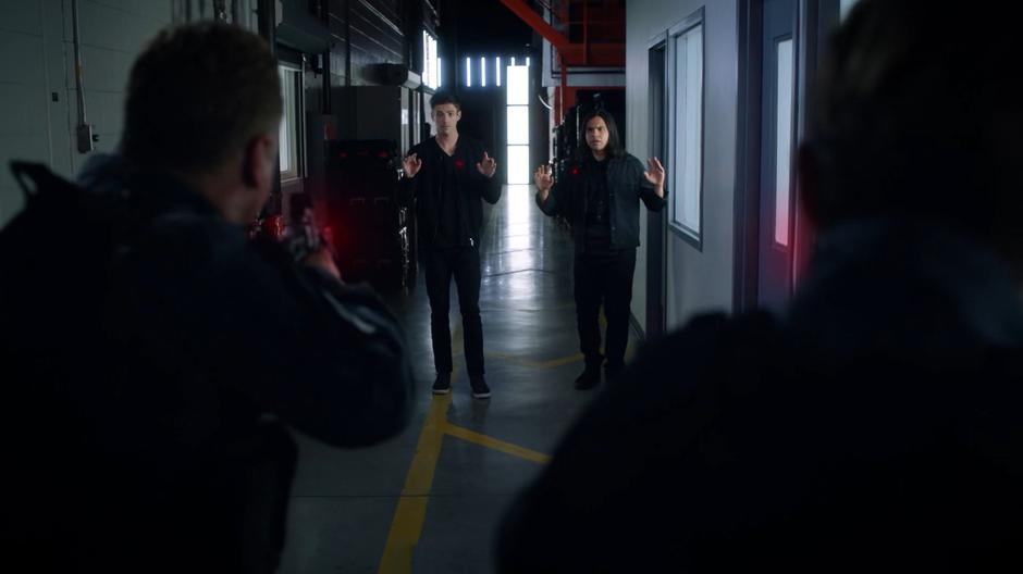 Two guards hold Barry and Cisco at gunpoint.