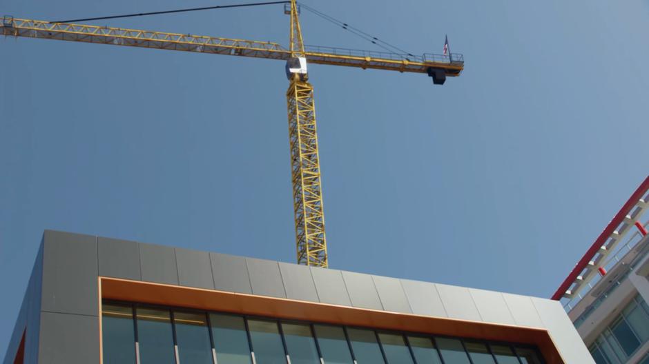 A crane tips over and falls towards the street.