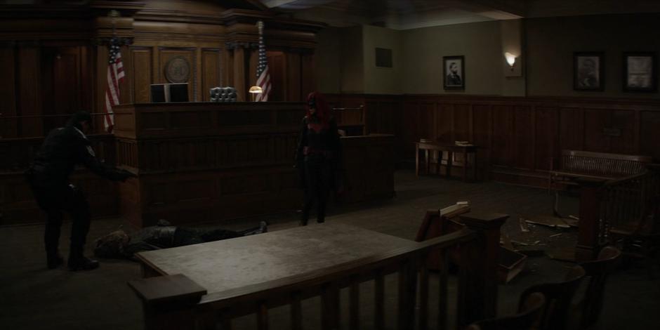 Jacob holds his gun on Kate as Batwoman while he kneels over the body of the Executioner.