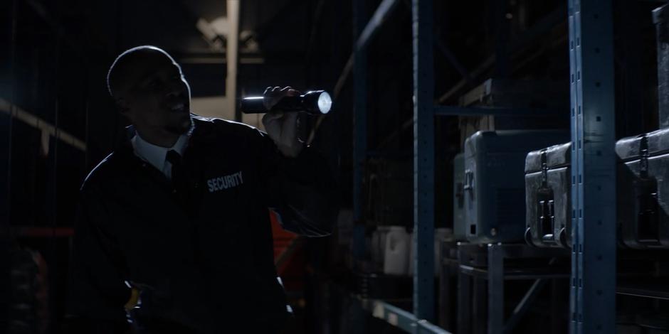 A security guard shines his flashlight through the shelves while attempting to flirt with Batwoman.