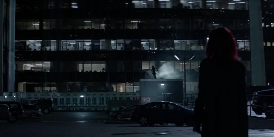 Kate watches from across the parking garage as a masked figure jumps down from above to stop the Rifle.