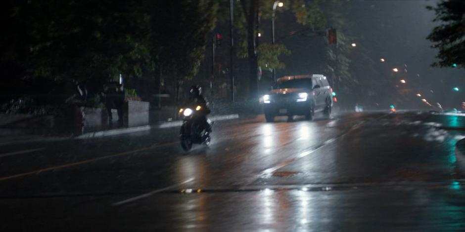 Kate races through the intersection on her motorcycle as the rain falls around her.