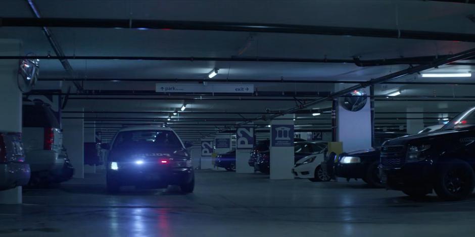 A police car speeds through the garage with its lights flashing.