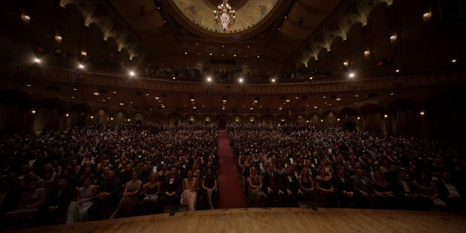 The audience members in the packed theater listen to Dr. Ethan Campbell introduce Catherine.