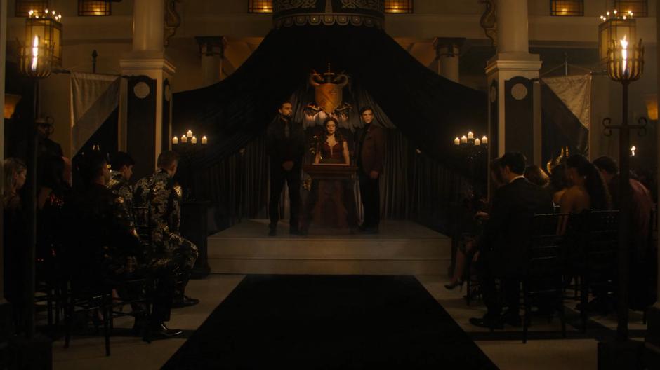 Godric stands on one side of Maggie and Parker on the other as the demons watch the wedding ceremony.