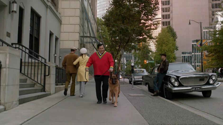 Dick Grayson walks down the sidewalk with his dog.