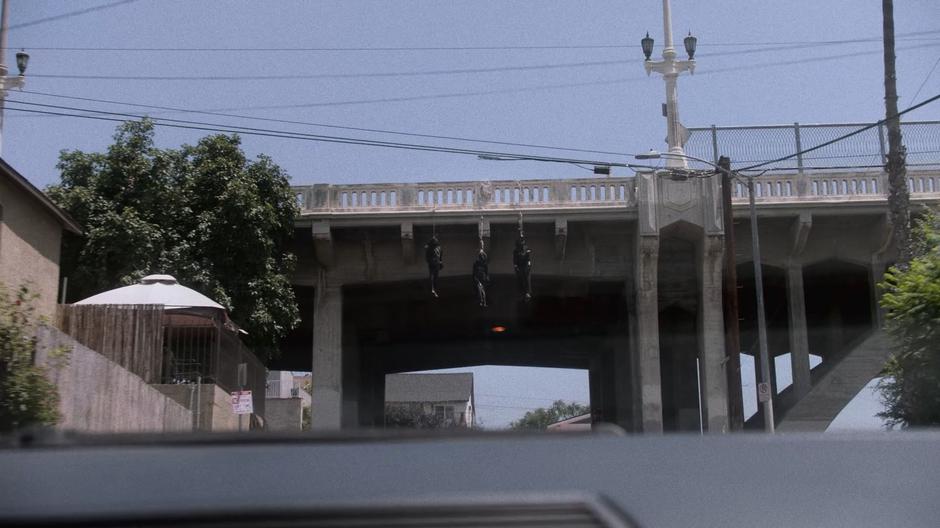 Three bodies hang from the bridge as the car drives beneath them.