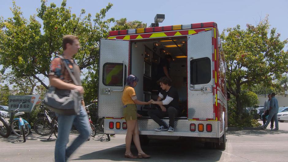 Gert holds Max's hand as he sits on the back of the ambulance.