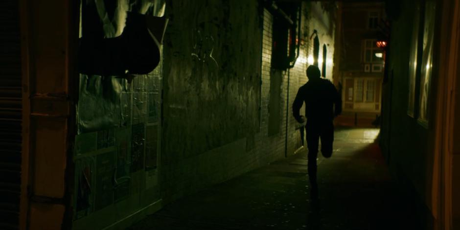 The spy runs down a dark alley towards his safe house.
