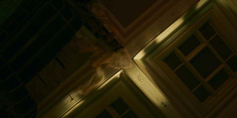 A strange figure emerges from the ceiling above the spy.