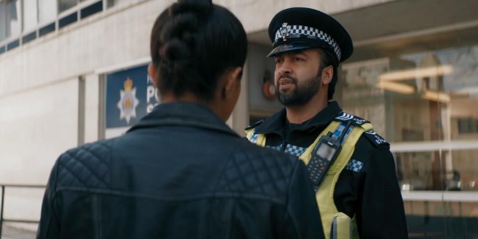 Ramesh looks over Yaz's shoulder at the two government agents waiting for her.