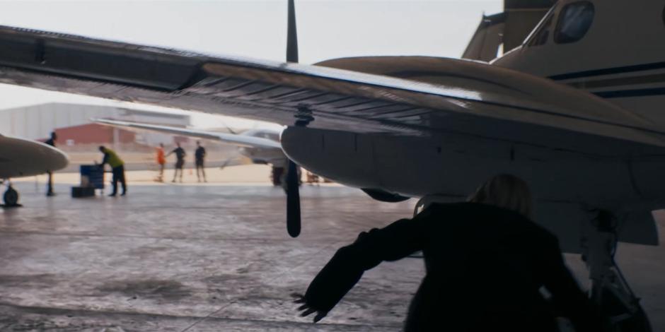 The Doctor ducks beneath the wing of a parked aircraft as she follows Daniel Barton stealthily.