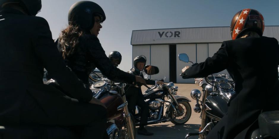 The gang pulls up in front the hanger on their motorcycles as the door closes.