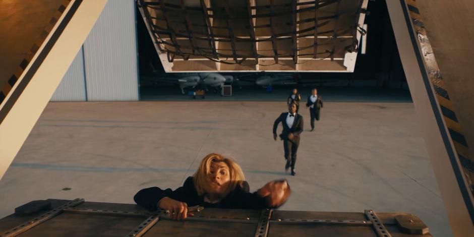 The Doctor climbs up onto the plane's cargo ramp as Ryan, Yaz, and Graham chase after her.