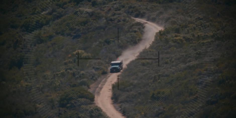 A truck drives down a dirt road in the sniper's scope.