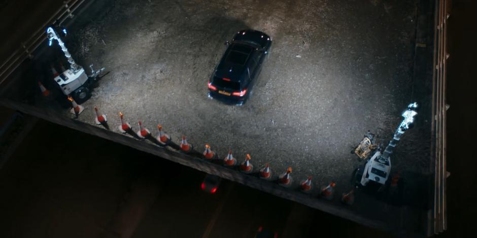The government vehicle drives towards the edge as cars speed past underneath.