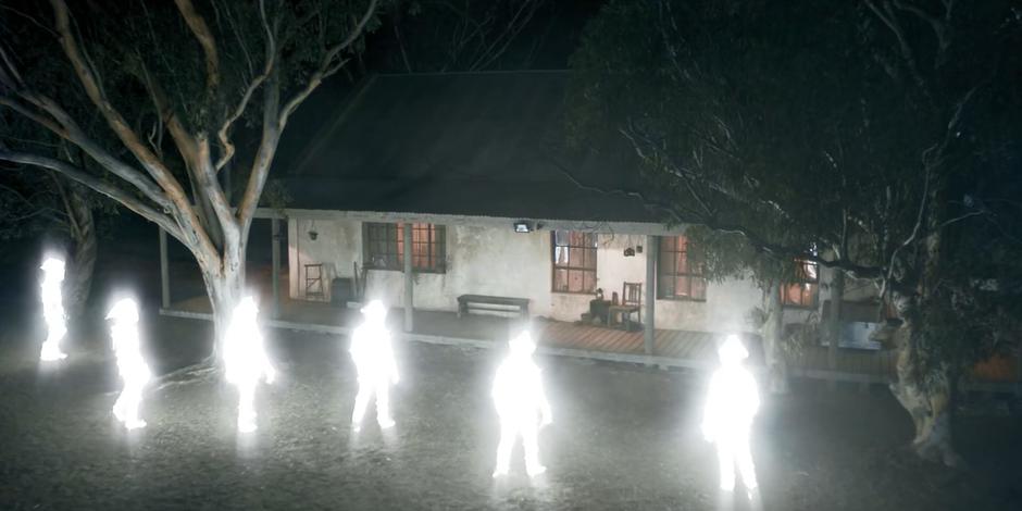 Six mysterious figures made of light approach the cabin.