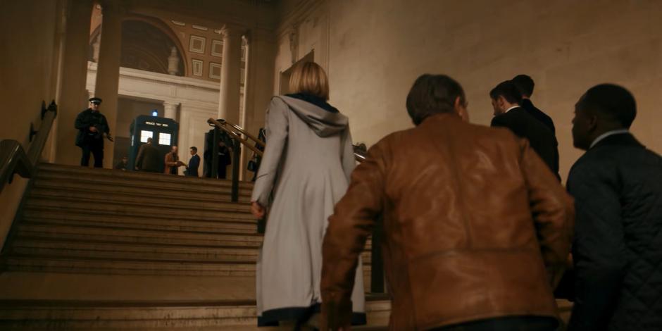 The Doctor, Graham, Ryan, and Yaz walk up the stairs to where some agents are unloading the TARDIS.