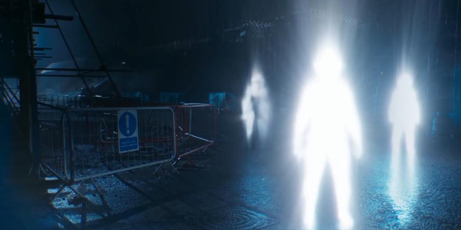 Three figures of light emerge from the ground.