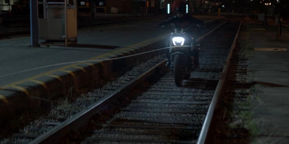 Kate rides her new motorcycle down the tracks and shoots her grappling hook at the train.