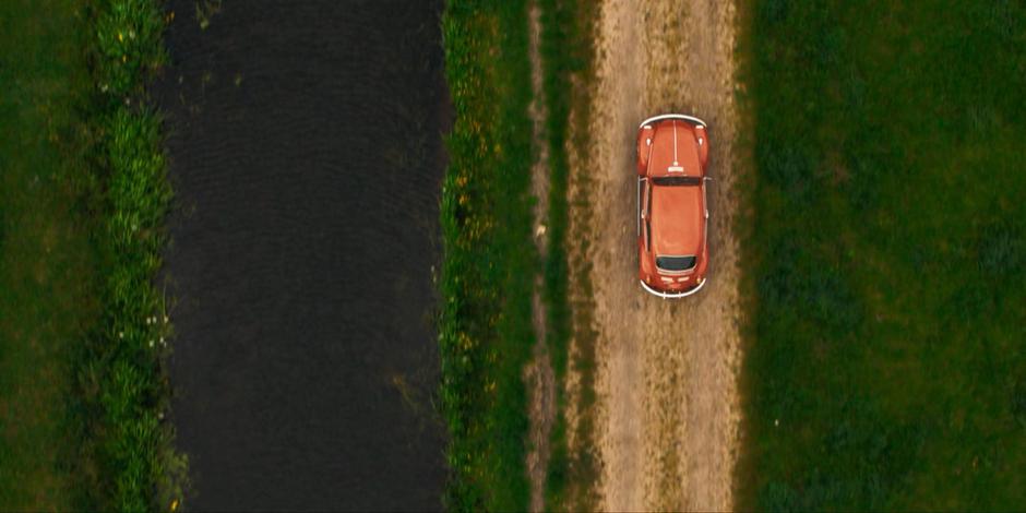 Ruth drives her VW Beetle down a dirt road past a canal.