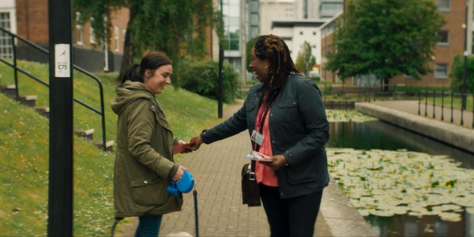 Ruth hands a flyer to a woman out walking her dog.