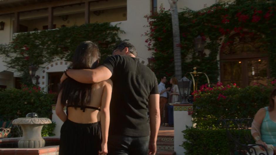 Robert puts his arm around Nico as they walk towards the main building of the hotel.