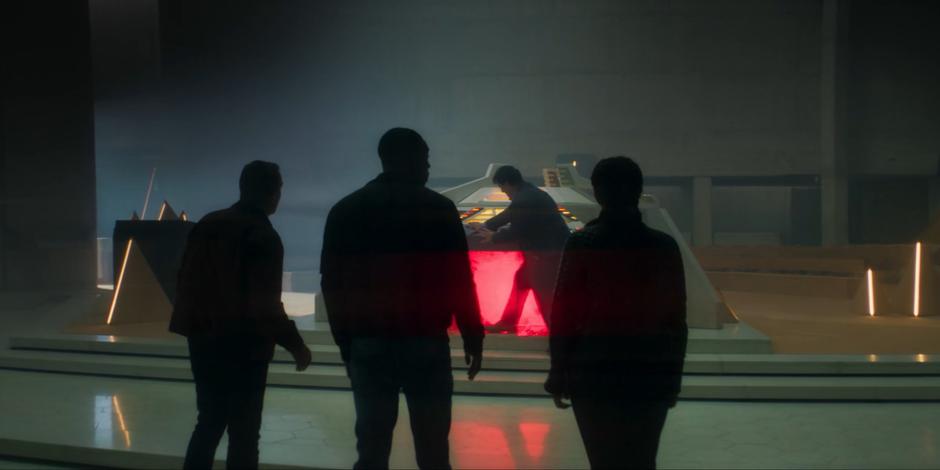 Graham, Ryan, and Yaz watch as Jack Harkness prepares the return teleporter for them.