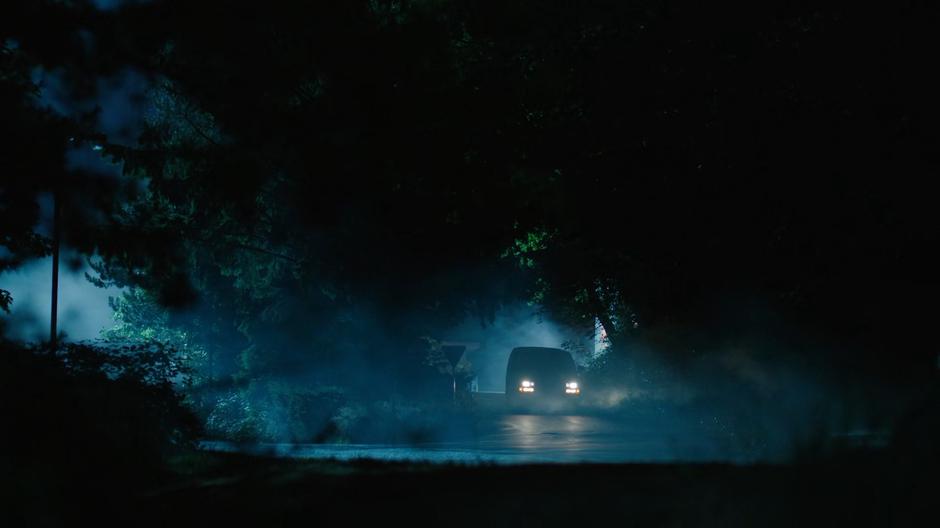 The coroner's van drives down a foggy road at night.