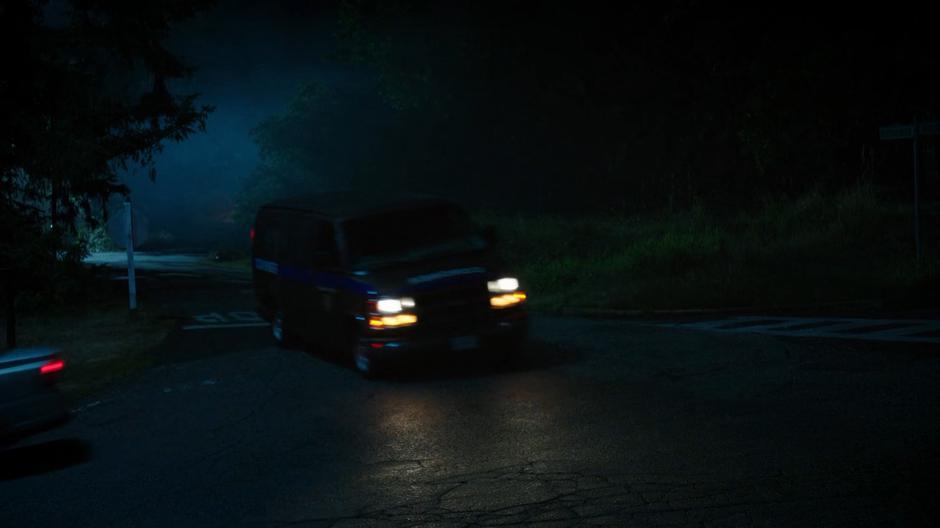 The coroner's van runs through a stop sign and barely avoids hitting another car.