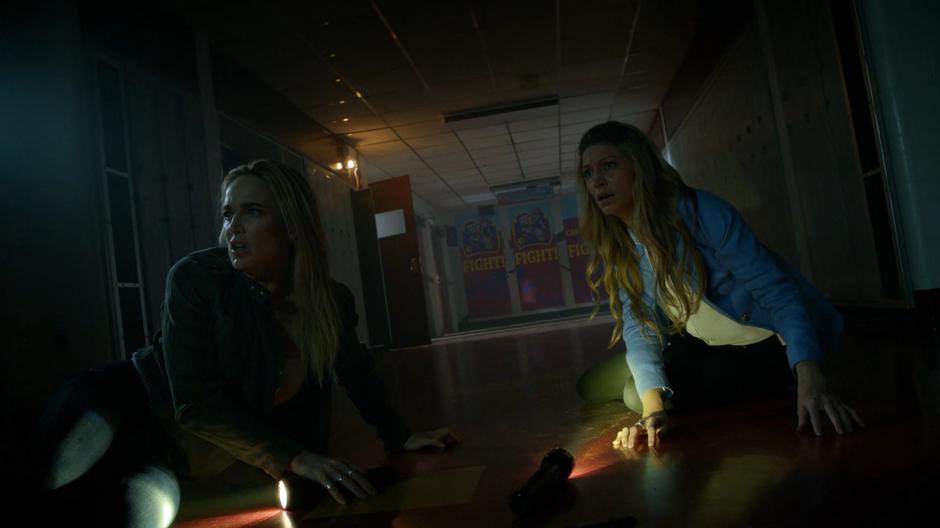 Sara and Ava look back down the hallway after being knocked down by the killer who crushed another student in a locker.