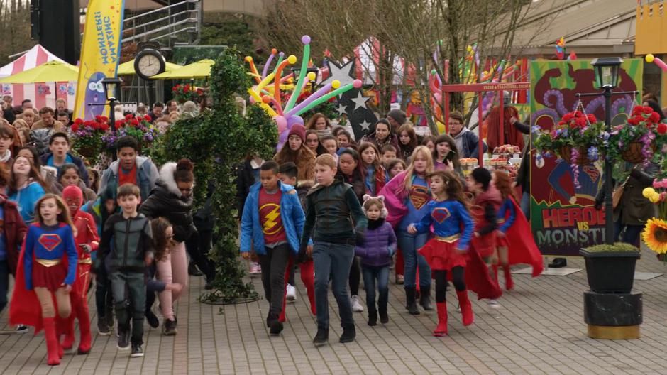 A group of kids dressed in Supergirl, Flash, and Green Arrow costumes run away from the Heroes vs. Monsters show after it is attacked.