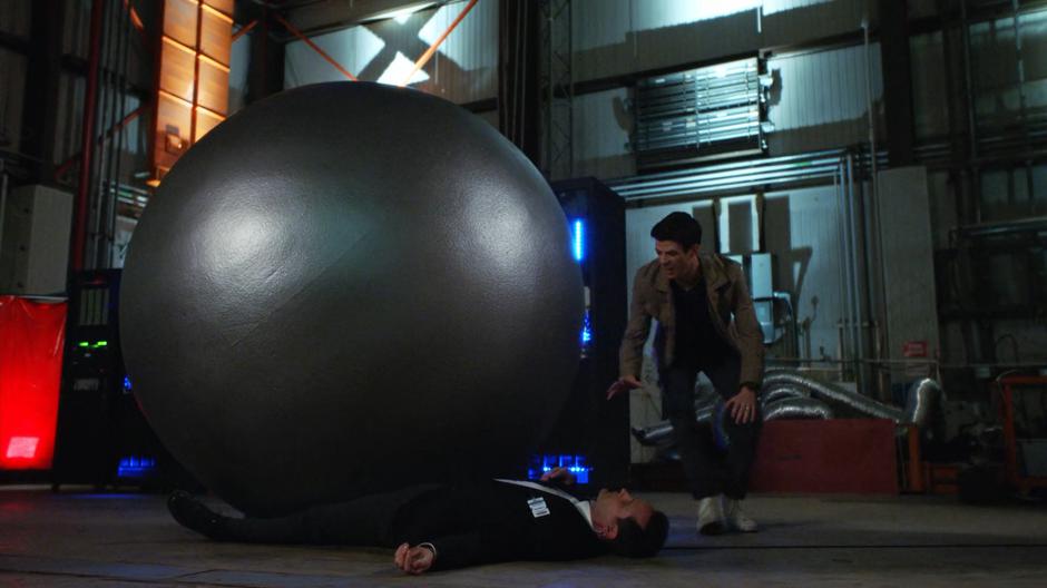Barry leans down to help the guard who is trapped beneath a giant sphere.