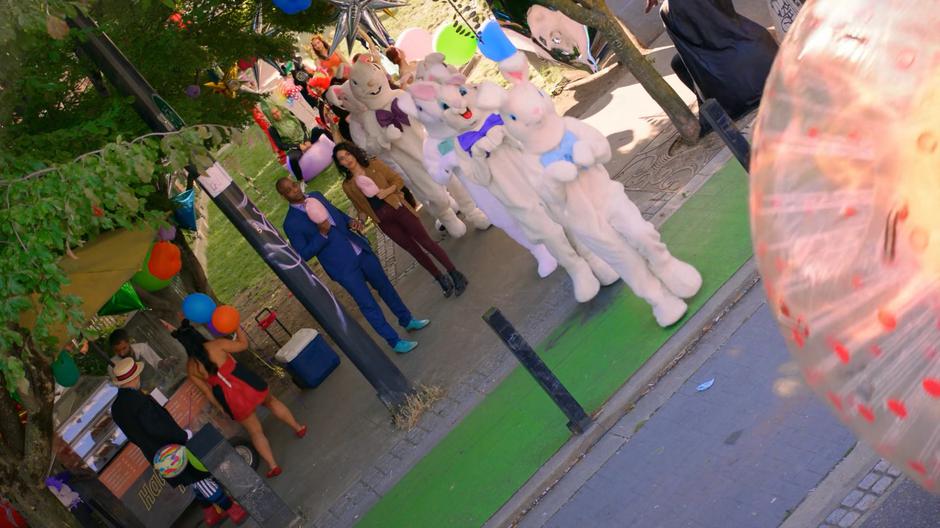 Fogg and Kady eat their cotton candy while a line of people in bunny suits hop past.