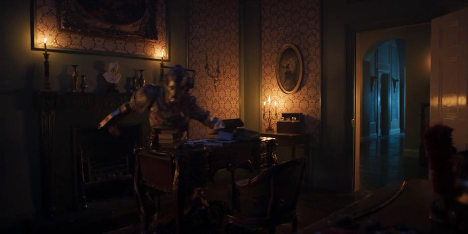 The Lone Cyberman pushes all of the books and papers off of Byron's desk.