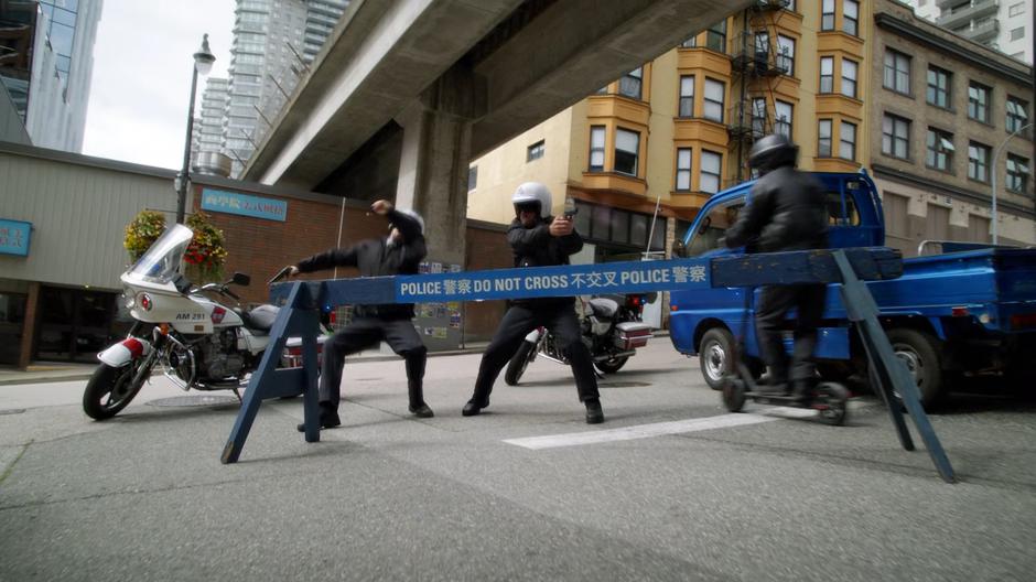 The police officers guarding the barricade try to stop the scooter-riding gang members from getting past.