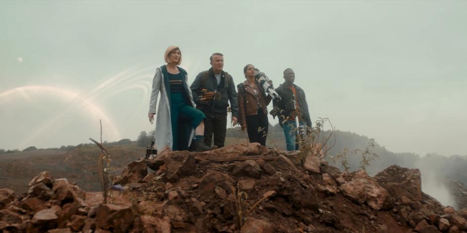 The Doctor, Graham, Yaz, and Ryan stand on the ridge looking down at the colony.