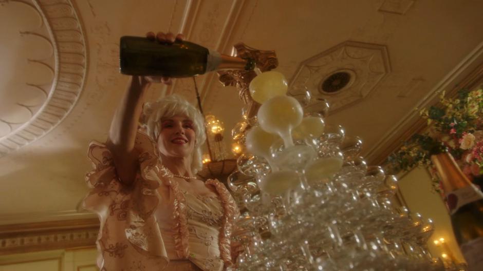 A woman pours champagne onto a tower of glasses.