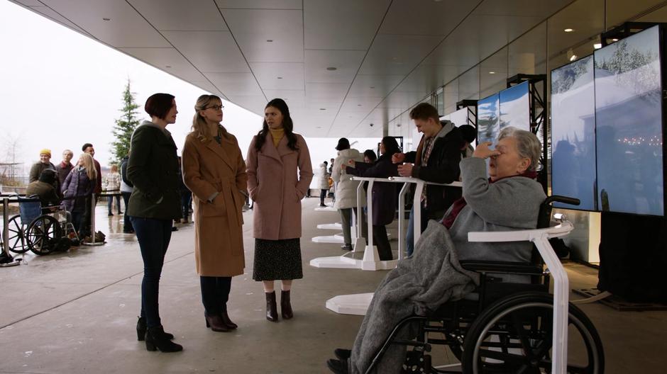 Alex, Kara, and Nia talk as a woman in a wheelchair exits the dragon simulation.